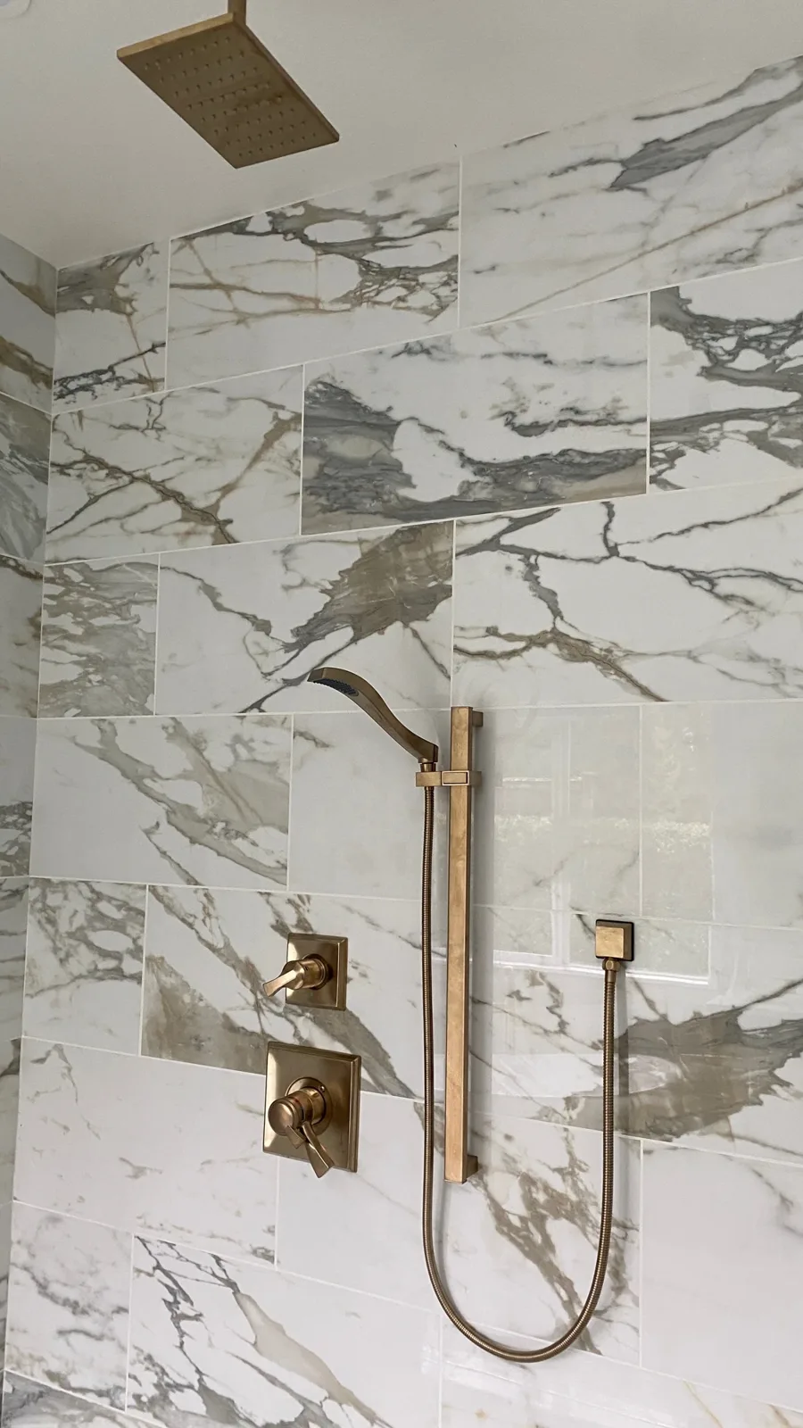 Brushed-gold ceiling rain head and handheld against calacatta-look shower tile