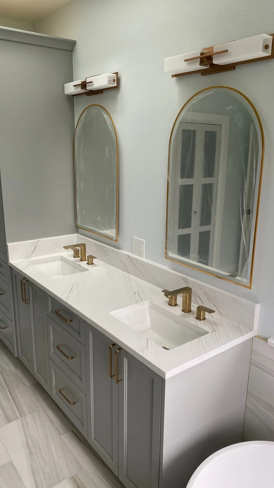 Double vanity with arched mirrors, quartz top, and brushed-gold faucets
