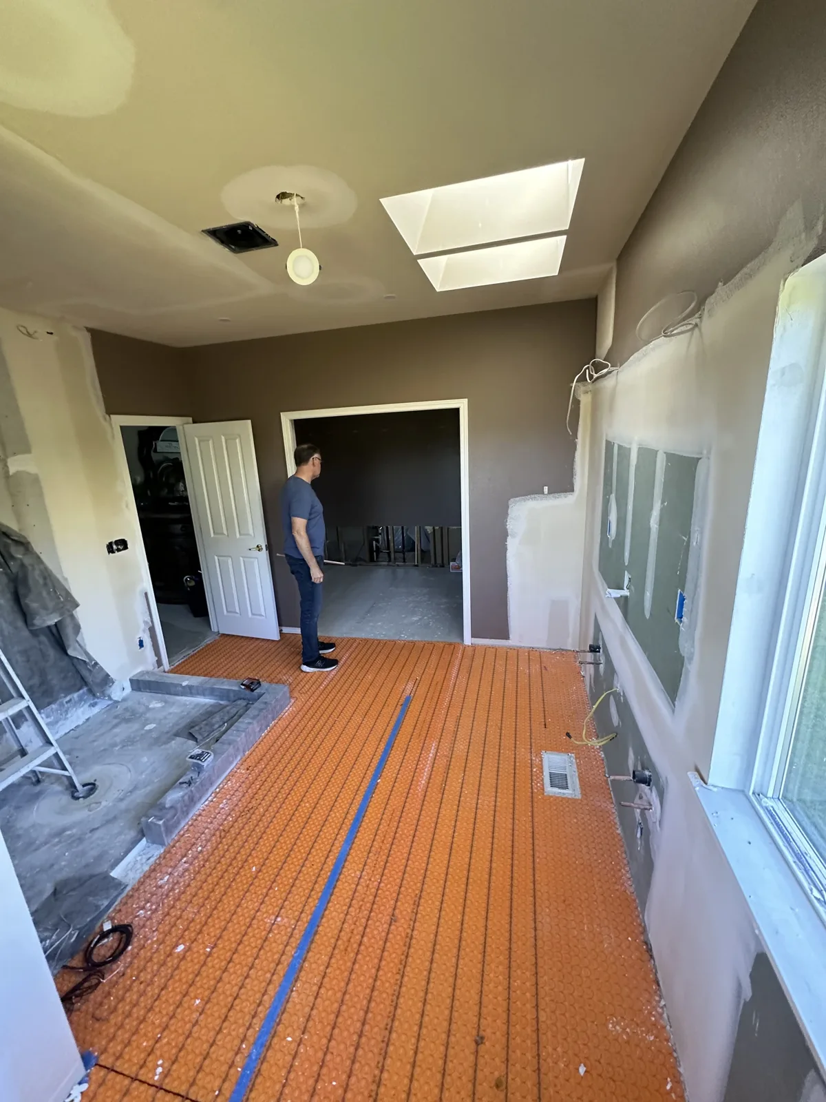 Heated-floor membrane laid across the room before tile, crew member at the doorway