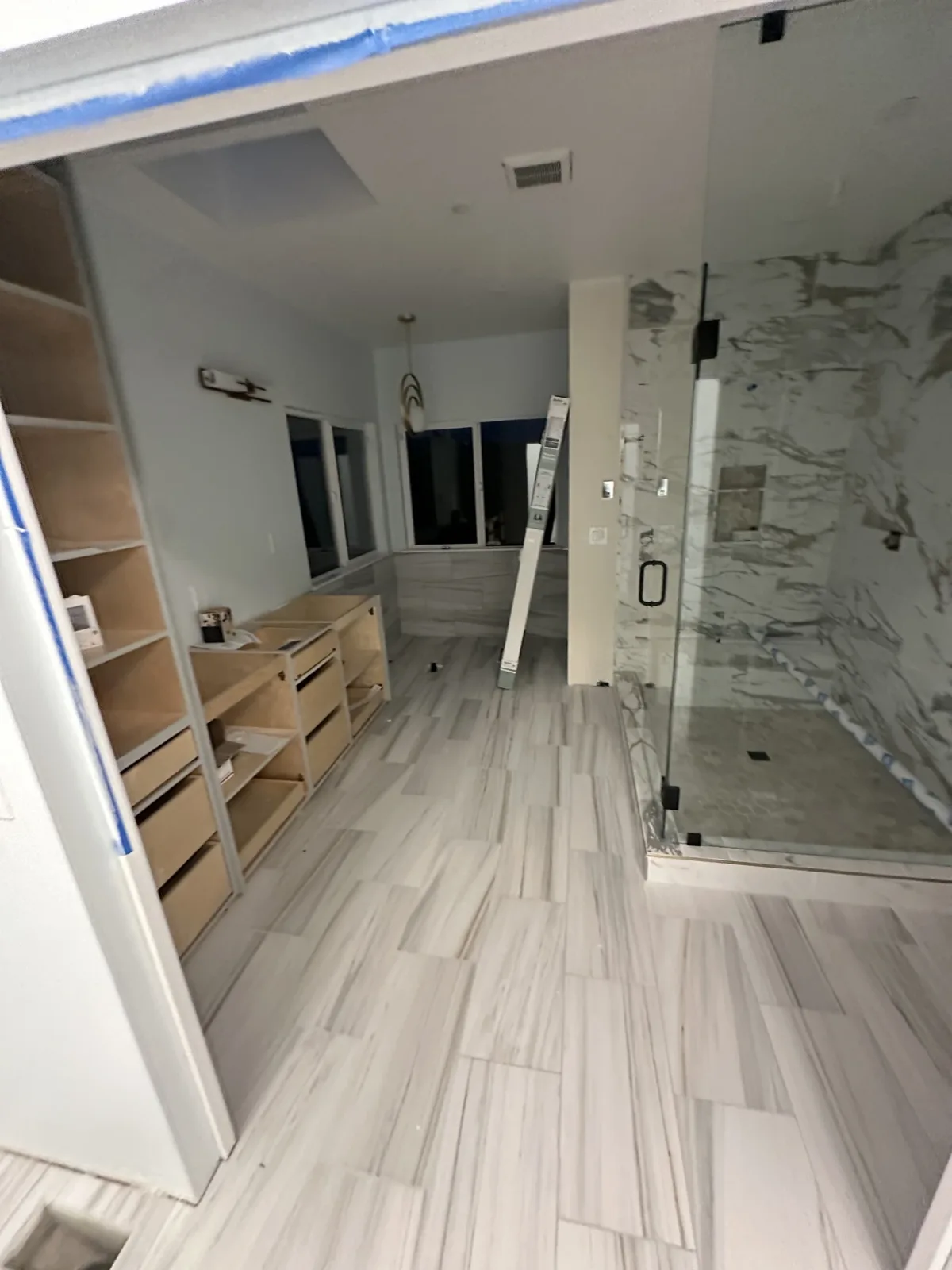 Vanity cabinets and shower glass in place with painter's tape at the ceiling