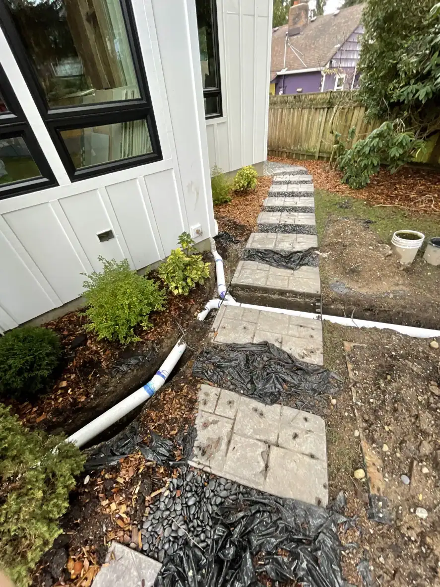 Side yard with a paver stepping-stone path and drainage set beside the house wrap