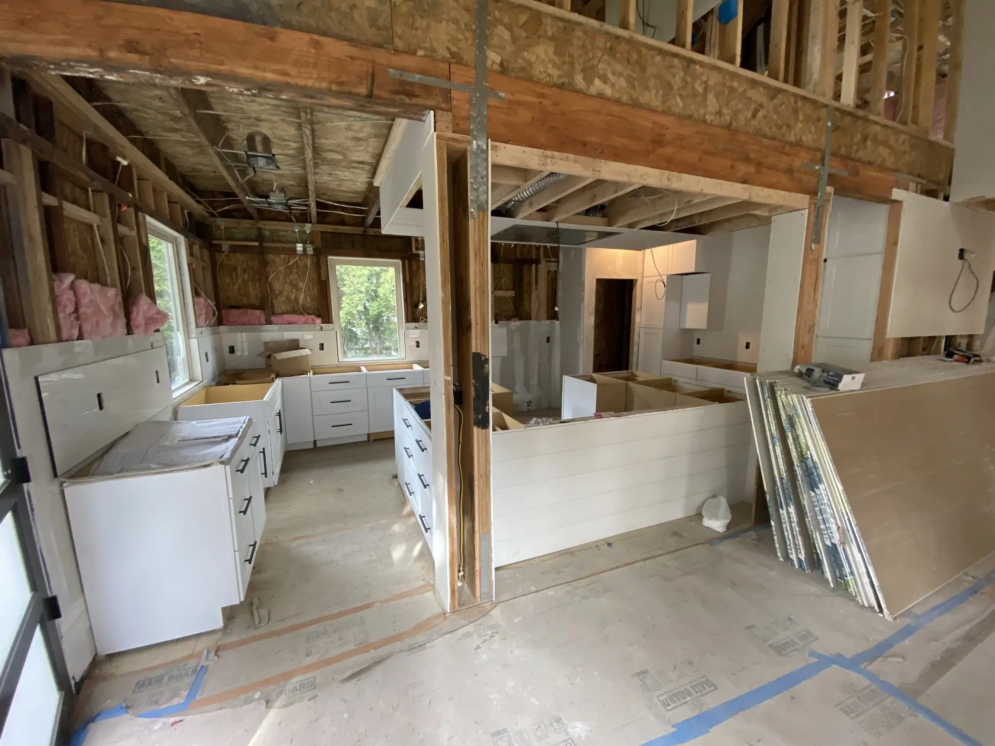 White kitchen cabinets set on the main floor at drywall stage, under protective covering