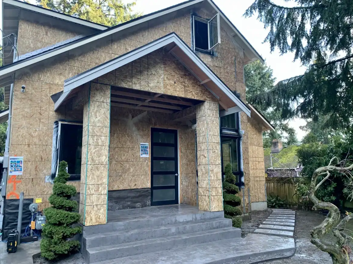 Front porch of the sheathed house with the black entry door and windows in place
