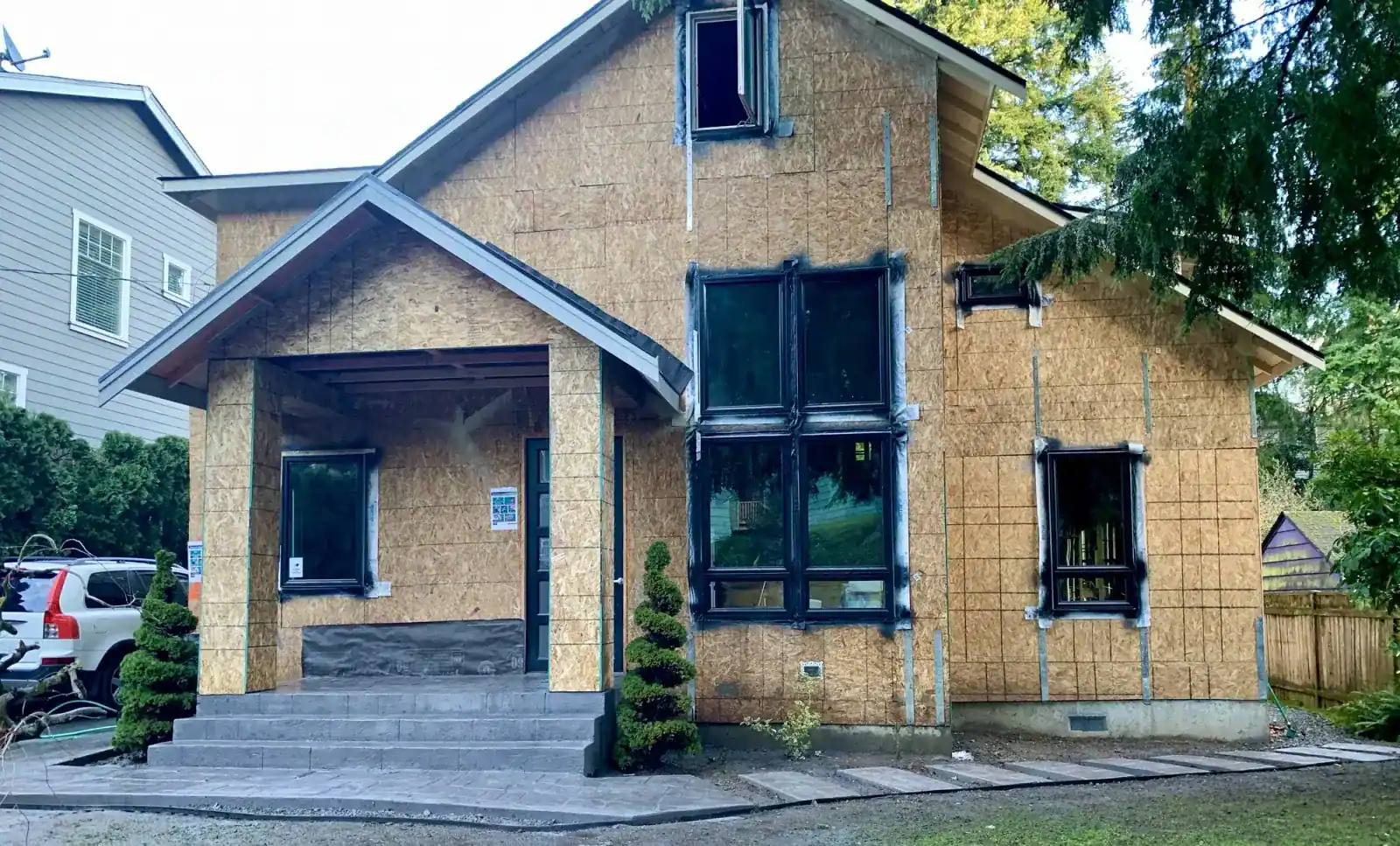 Sheathed front gable with black windows installed and the entry porch framed
