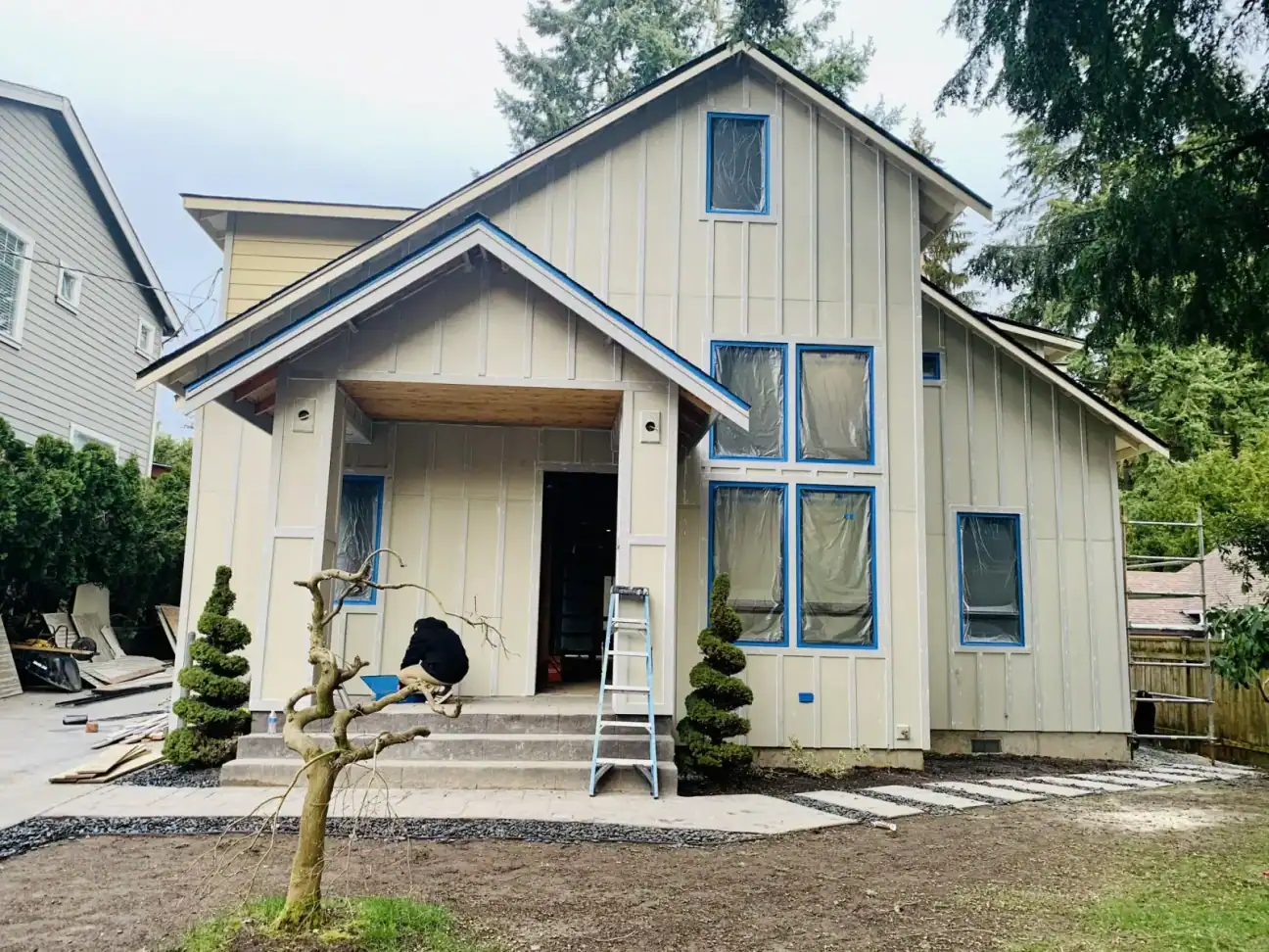 Front gable of the new home in white board-and-batten with windows taped and trimmed during siding