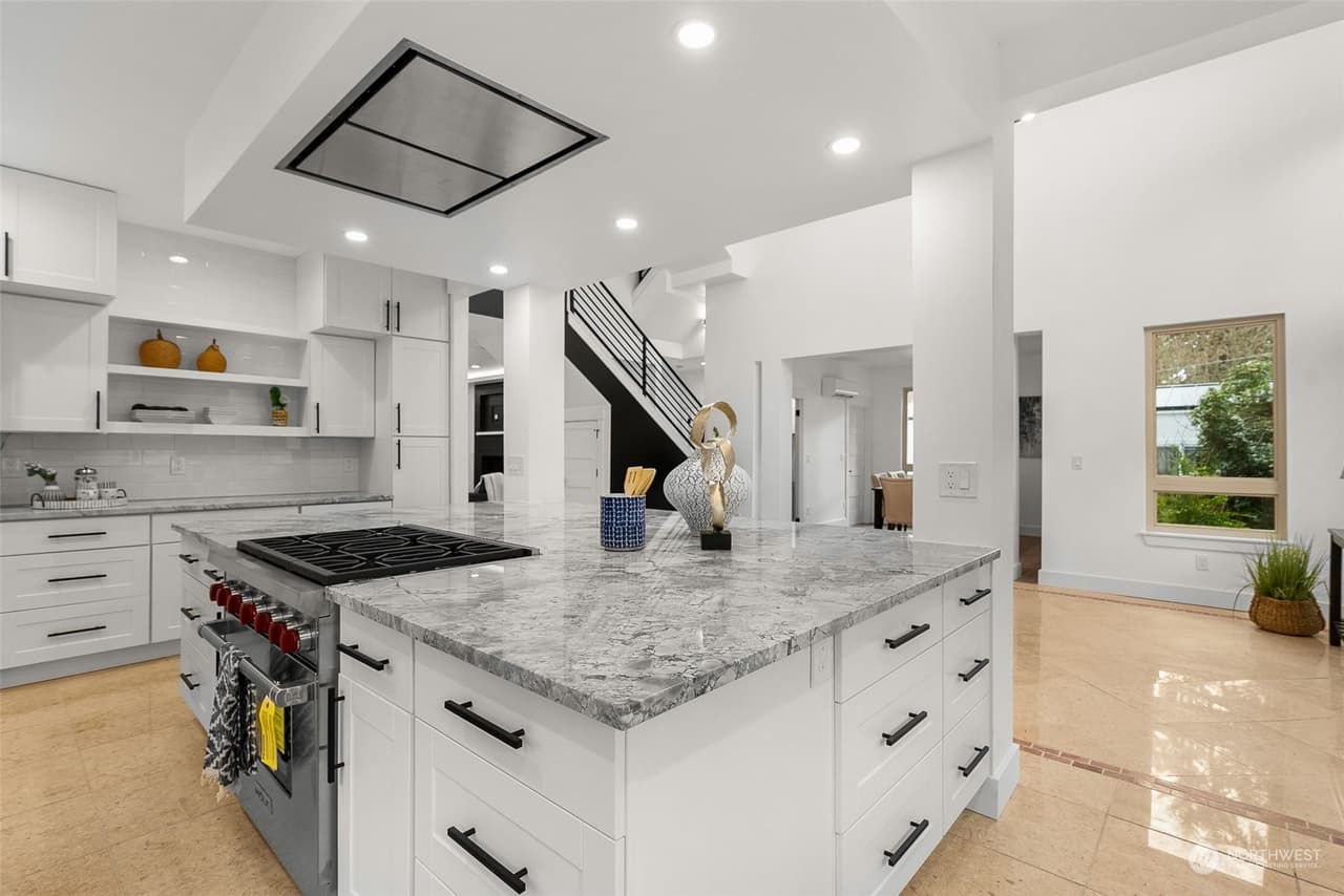 Kitchen island with a pro-style range, marble-look quartz, white shaker cabinets, and a range hood