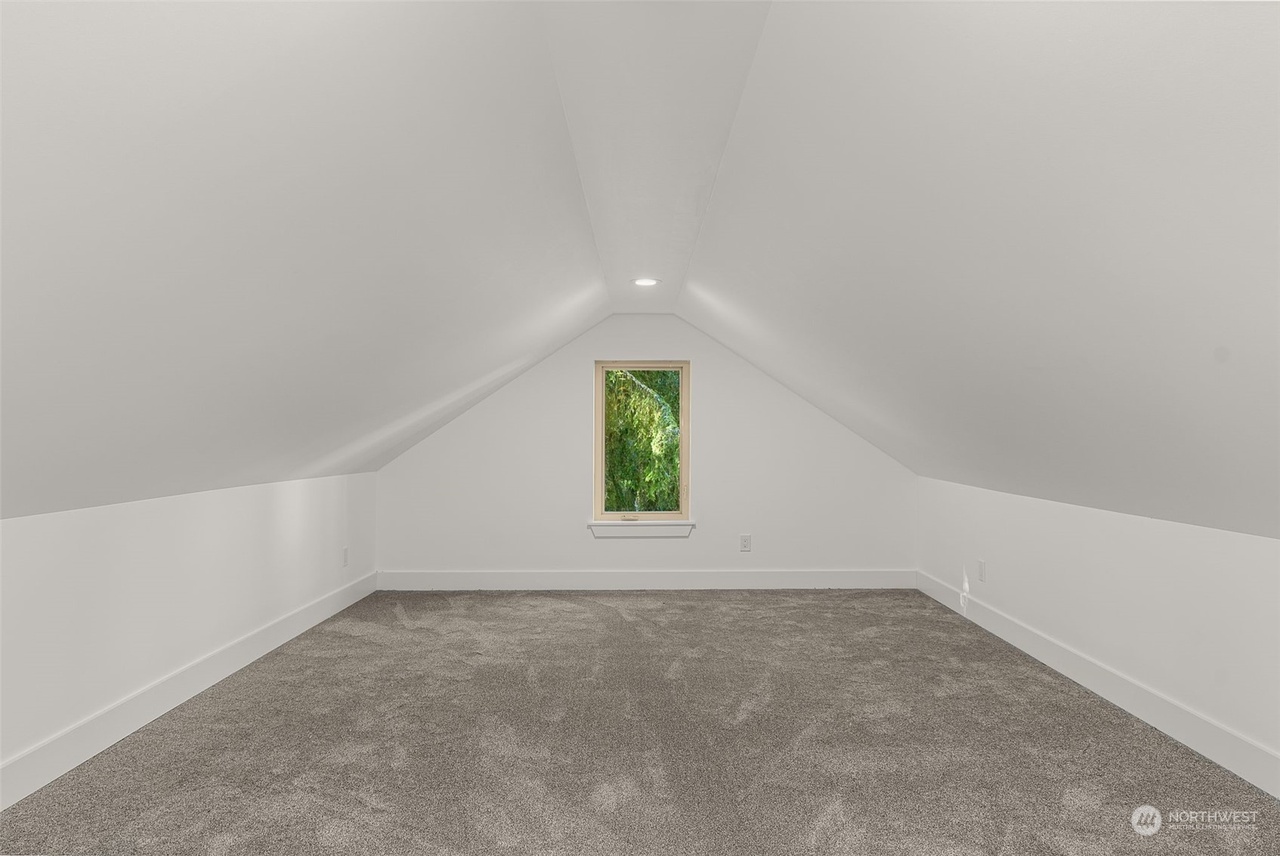 Carpeted bonus room under the vaulted roof with a small gable window