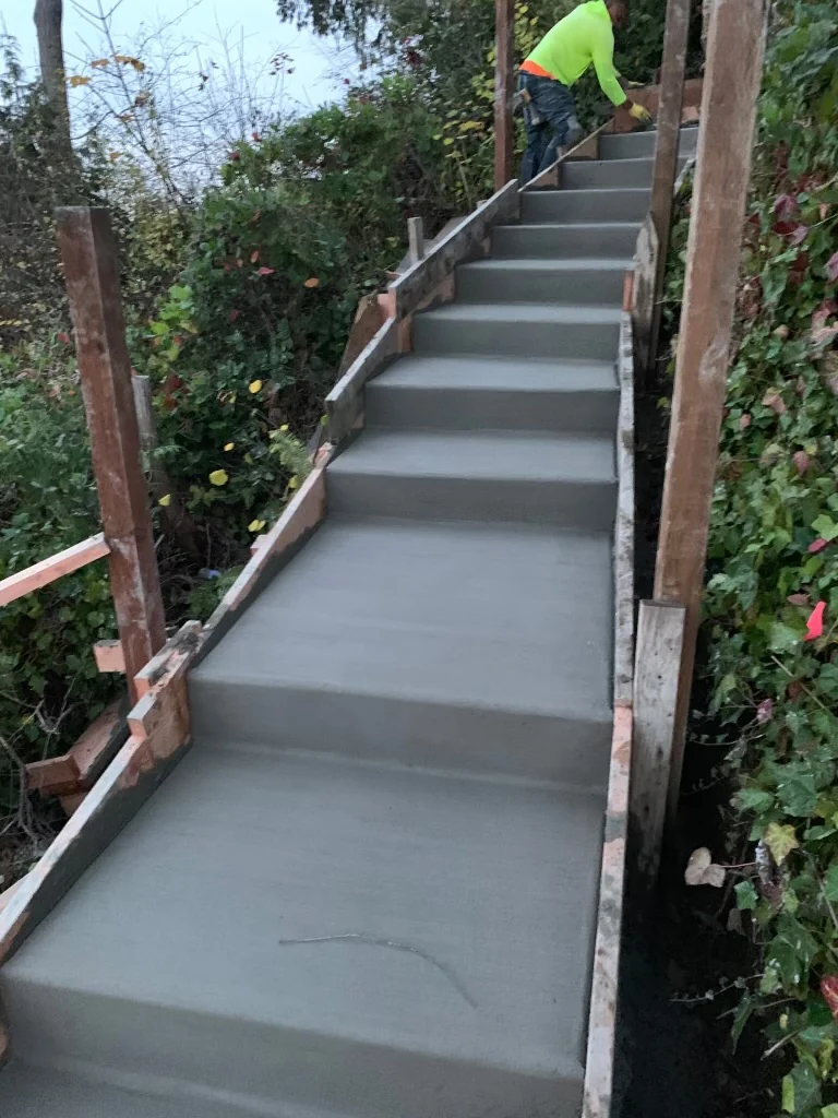 Freshly poured, broom-finished concrete stair with a crew member at the top