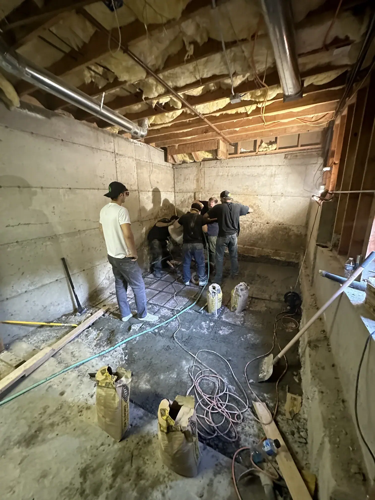 Crew standing in the lowered basement with rebar laid out below the exposed joists