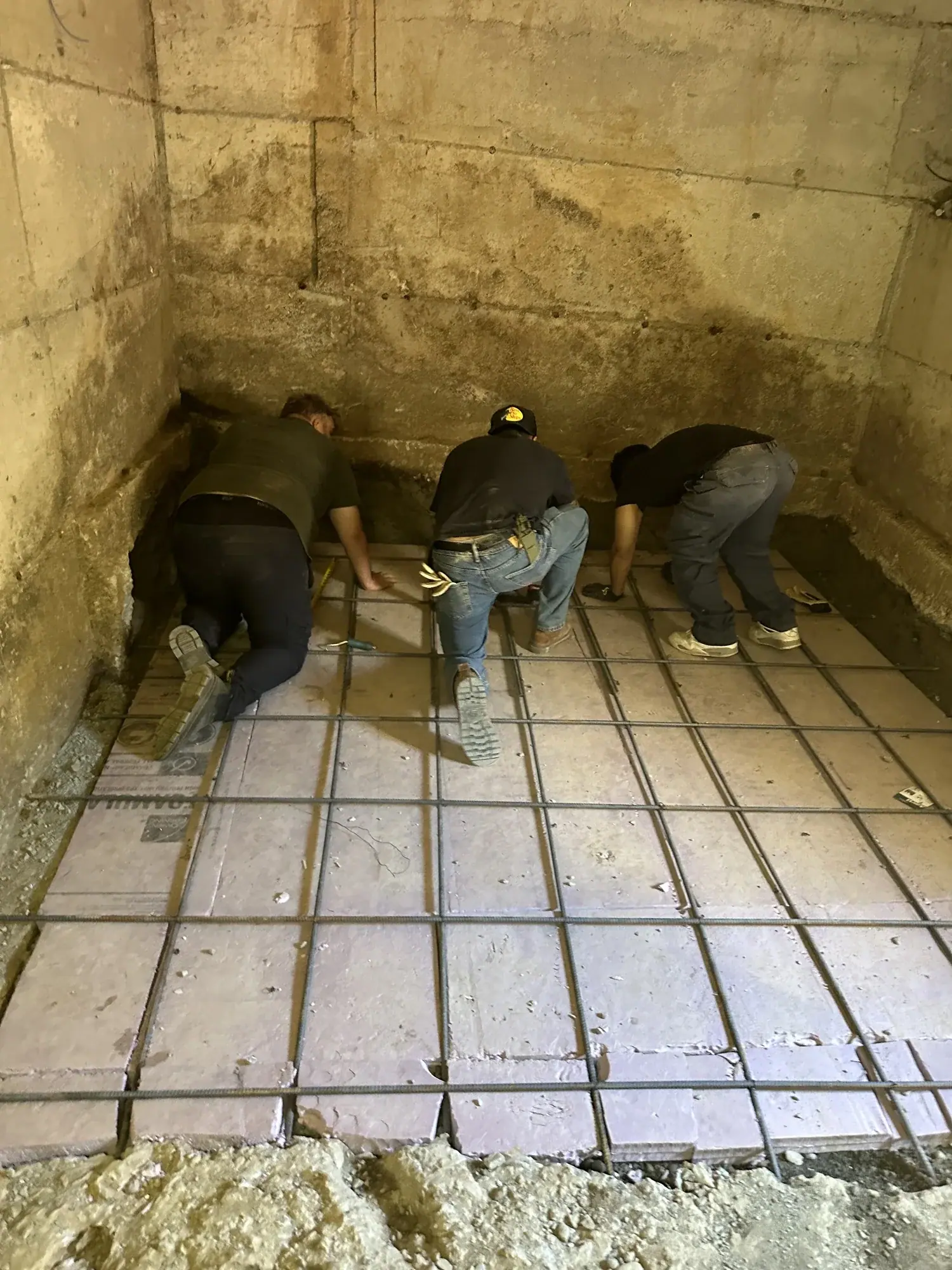 Three crew members tying the rebar grid over a gravel base for the new structural slab