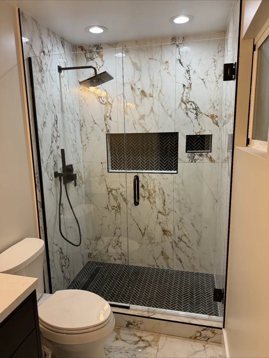 Marble-look tile shower with matte-black fixtures behind a glass door