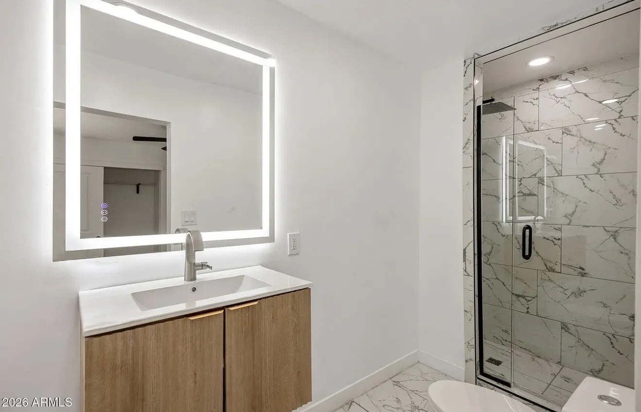 Bathroom with an LED mirror, floating wood vanity, and glass marble-tile shower