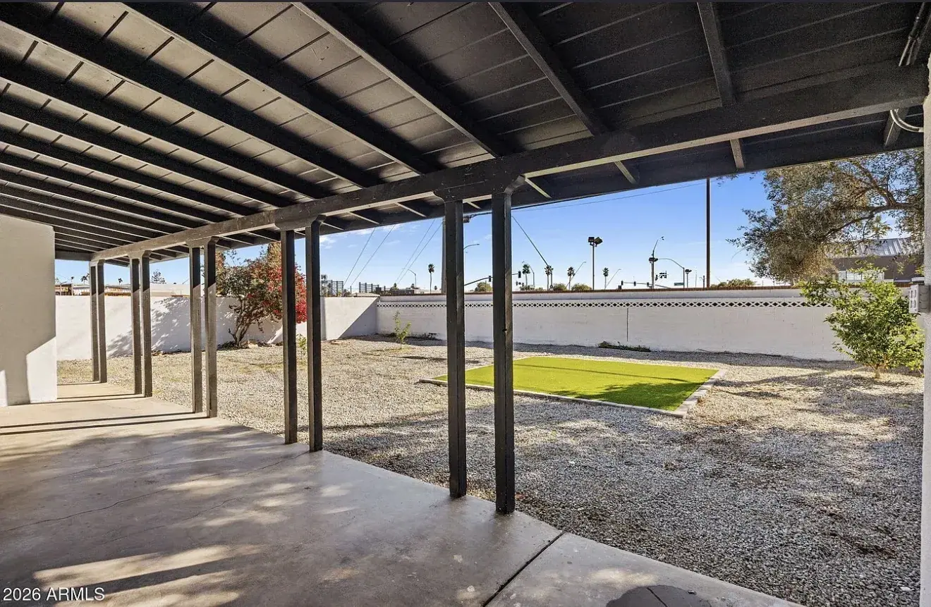 Covered back patio with black-painted beams looking over gravel and new turf